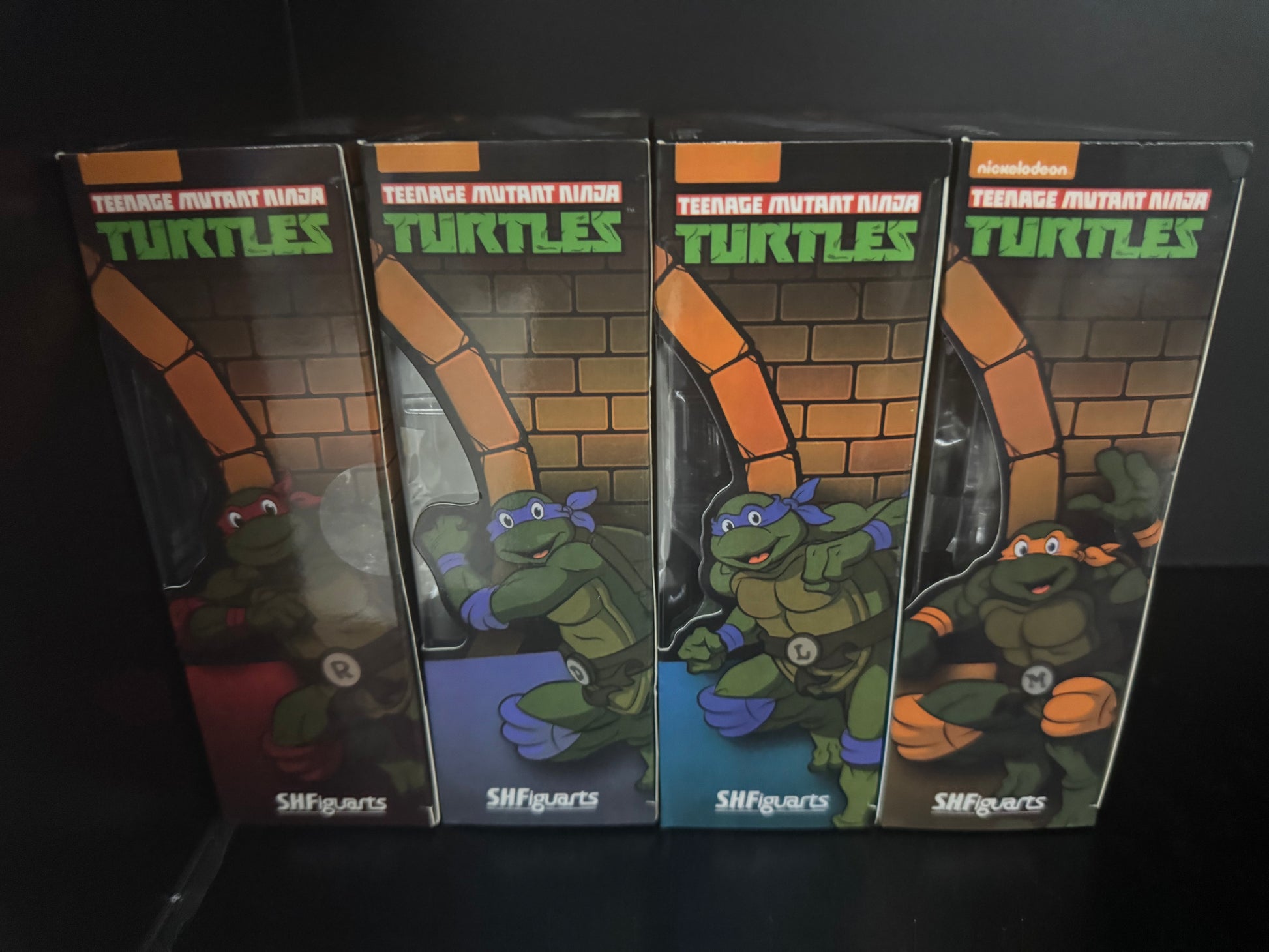 Four Teenage Mutant Ninja Turtles SHIFigarts action figure boxes lined up on a black background. The boxes feature illustrations of Leonardo, Donnie, Michelangelo, and Raphael.