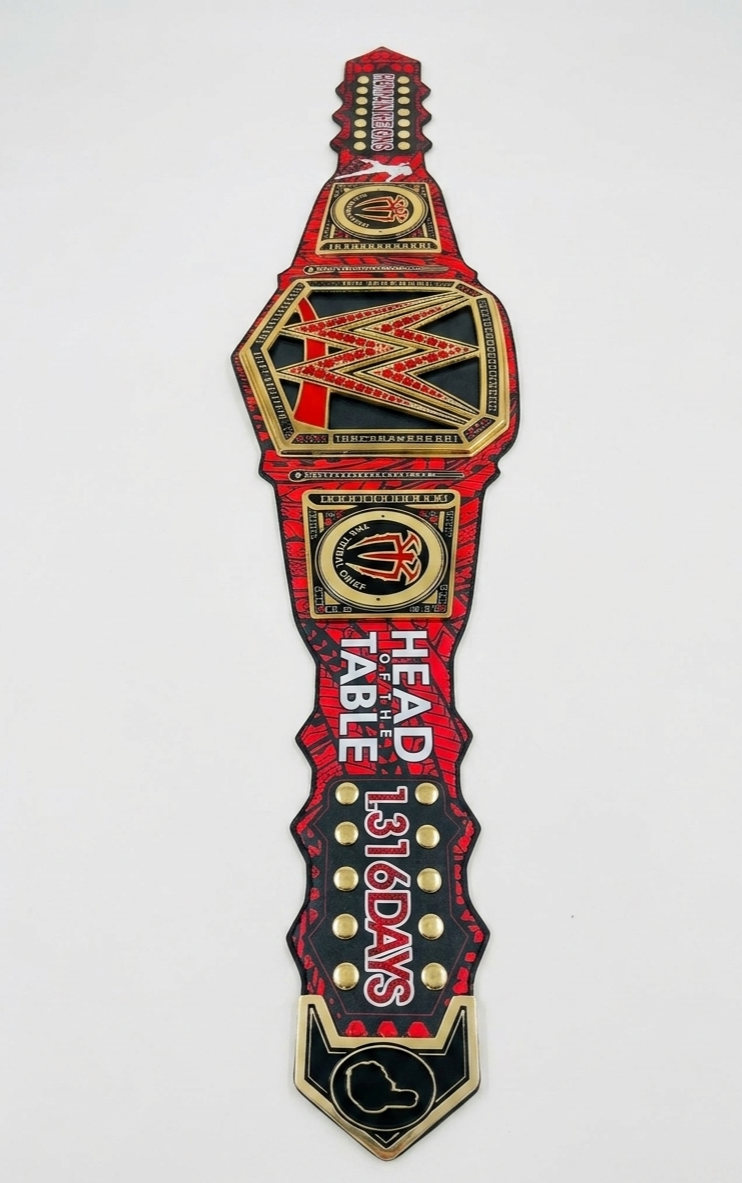 A WWE Championship belt replica or patch featuring red, black, and gold colors with the text 'HEAD TABLE 136 DAYS' and the WWE logo.